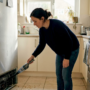 Woman vacuuming refrigerator coils in kitchen